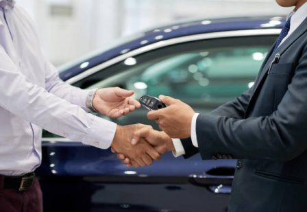 Salesman giving car keys to customer and shaking his hand